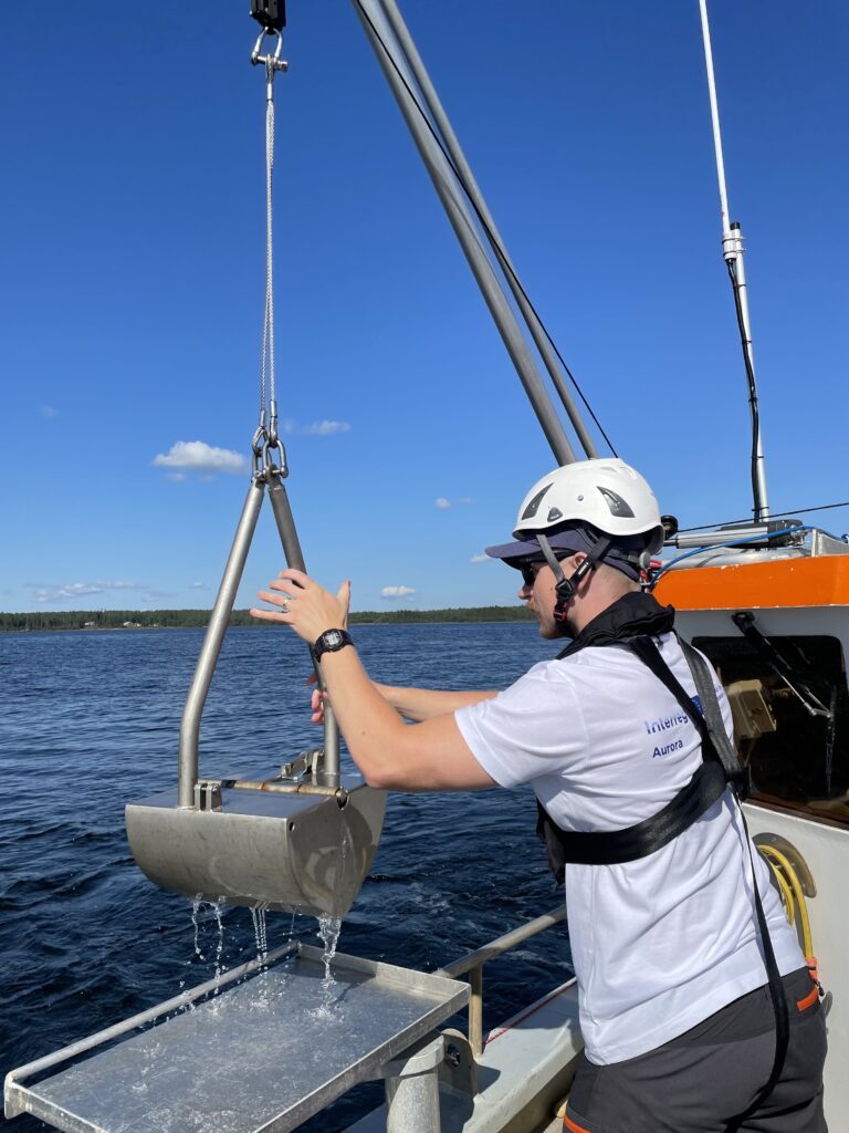 Person onboard the boat holding the sediment sampler 